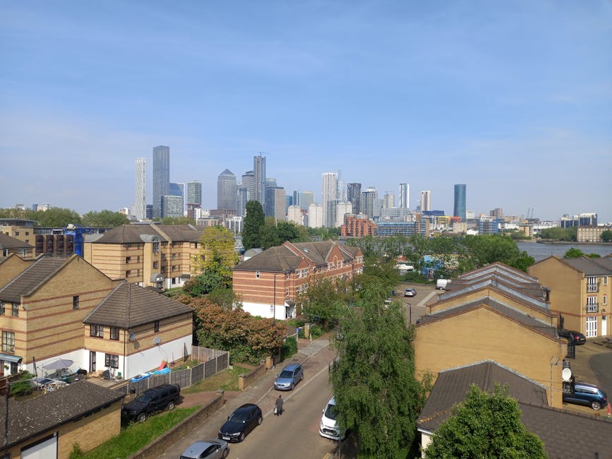 A wide view of the Canary Wharf skyline featuring several modern high-rise office buildings with reflective glass facades, including a distinctive twisted steel structure on the left and a tall, recta