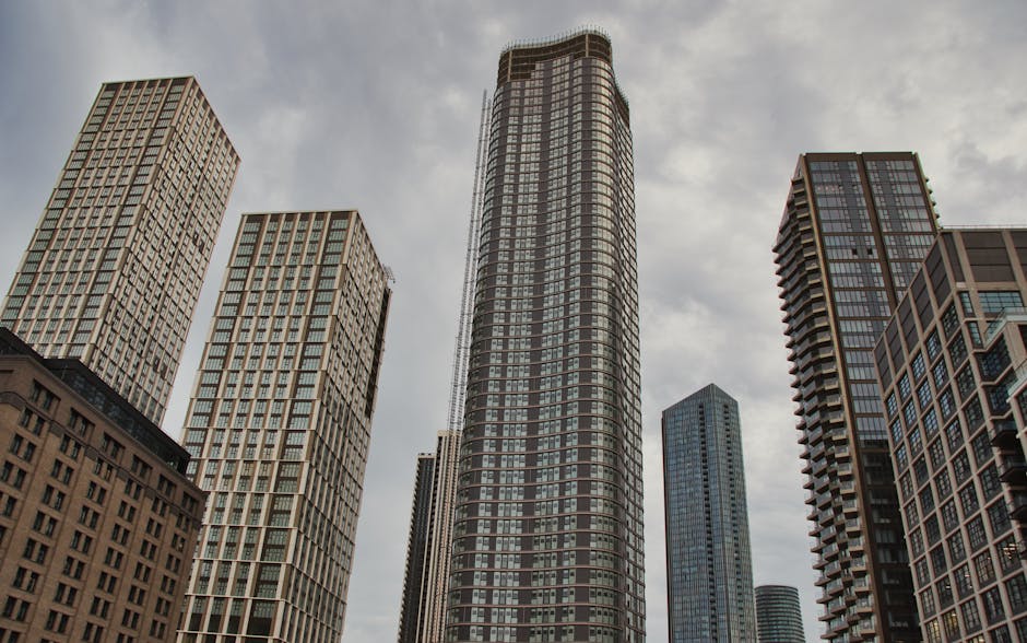 A black and white photograph of a modern city skyline with multiple high-rise buildings of various architectural styles. The buildings, made of glass and steel, include tall, sleek towers with reflect